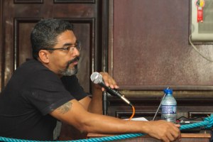 A man with glasses and a beard speaking into a microphone