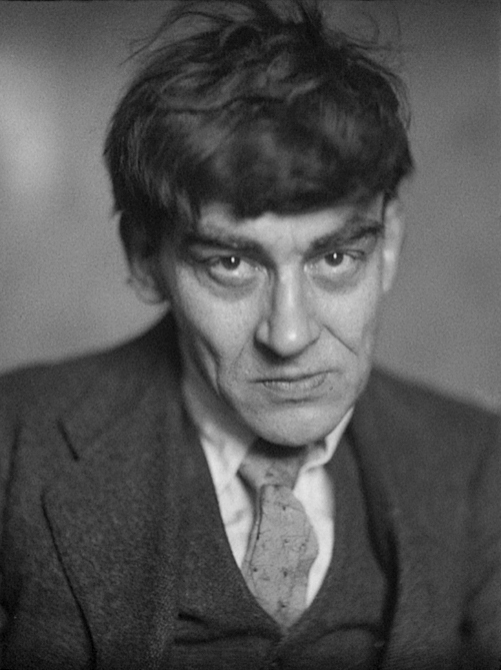 Black-and-white close-up portrait of a man with messy dark hair, intense gaze, looking at camera