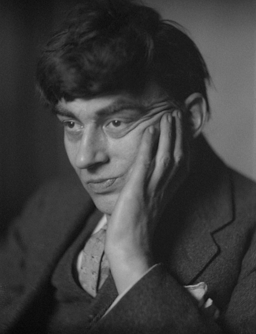 Black-and-white close-up portrait of a man with messy dark hair, resting chin on hand, looking sideways