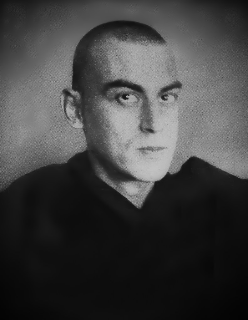 Close-up black-and-white portrait of a man with a shaved head, staring intensely at camera