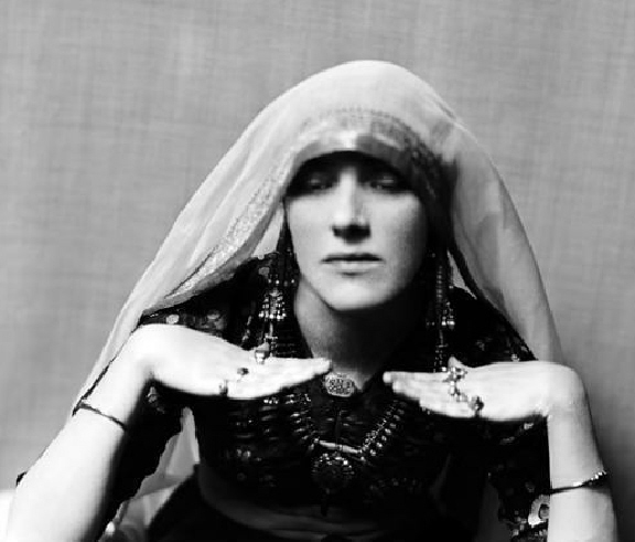 Vintage black-and-white photograph of a veiled woman with elaborate jewelry performing a ritual gesture