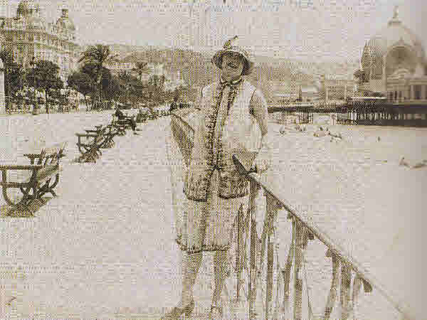 Vintage sepia photograph of a woman in a cloche hat and patterned dress on coastal promenade