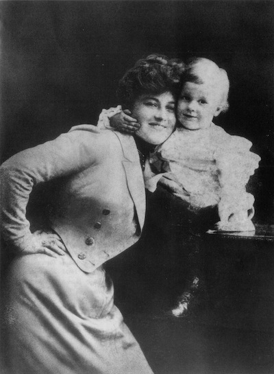 Vintage black-and-white studio portrait of a smiling woman in jacket embracing child on table