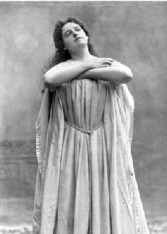 Vintage black-and-white photograph of a woman in a flowing gown, arms crossed, looking upward