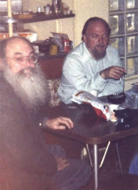 Two men with beards sitting at a table in a simple room