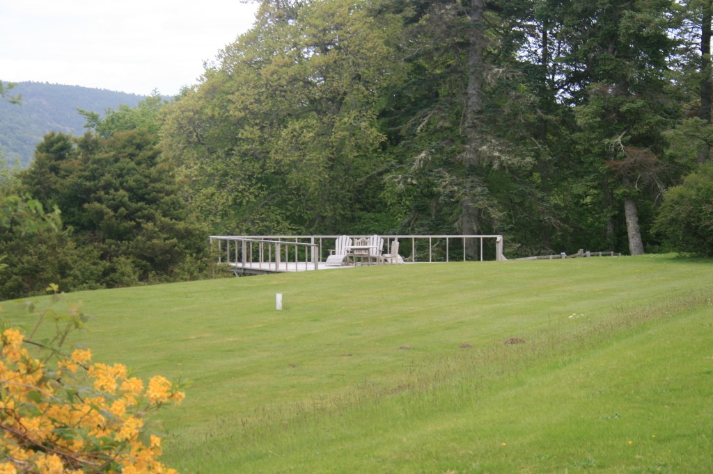 Wide landscape view of long, white single-story Boleskine House with bay windows on green slope