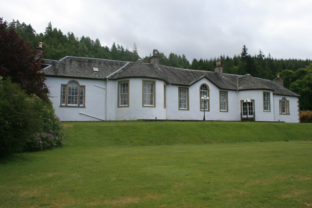 Wide exterior view of single-story white Boleskine House with slate roof on green lawn
