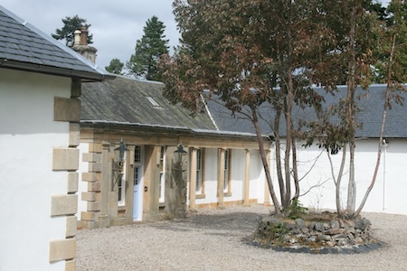 Boleskine House with stone pillars, light blue doors, gravel courtyard, and small stone-ringed tree