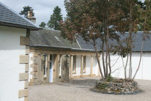 Boleskine House with stone pillars, light blue doors, gravel courtyard, and small stone-ringed tree