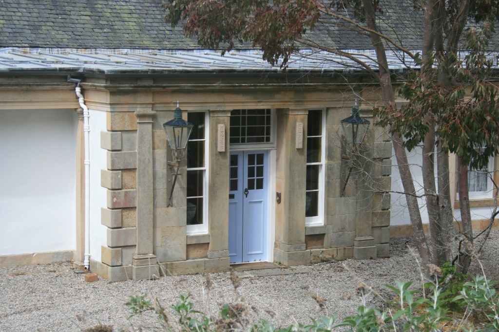 Boleskine House with stone pillars, light blue doors, traditional lanterns, and gravel driveway
